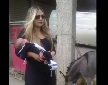 Family photograph of Serena holding her baby on a street in Lebanon, a donkey beside them.