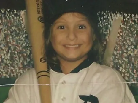 Family photograph of Serena as a young girl in a Detroit Tigers baseball uniform, smiling with a bat over her shoulder.