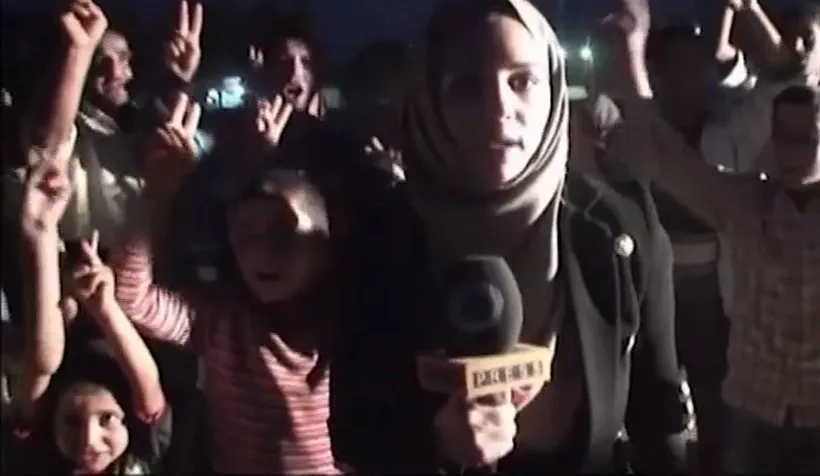 Serena reporting at night among residents near Suruç, a Press TV microphone in hand, hands raised in V-signs behind her.