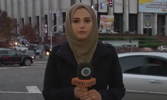 Serena reporting from a street in Ukraine, a billboard with Ukrainian text behind her, 2014.