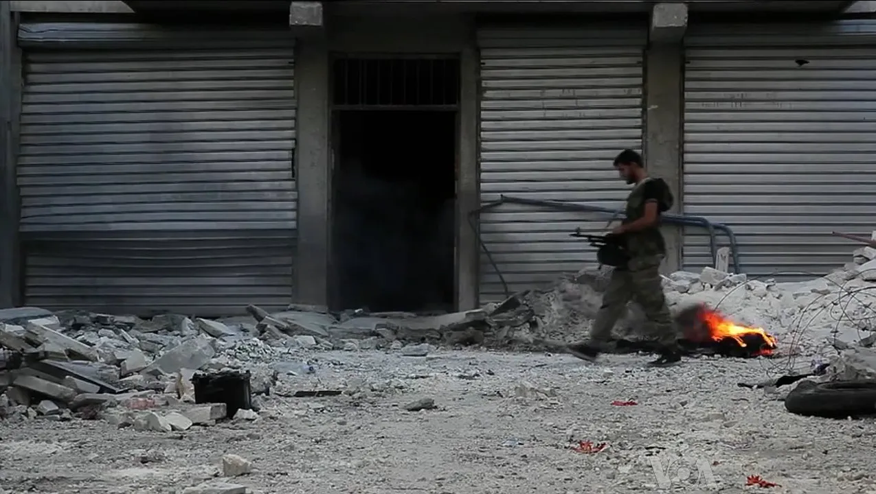 A fighter walking through rubble past shuttered storefronts in Aleppo, Syria, 2012.