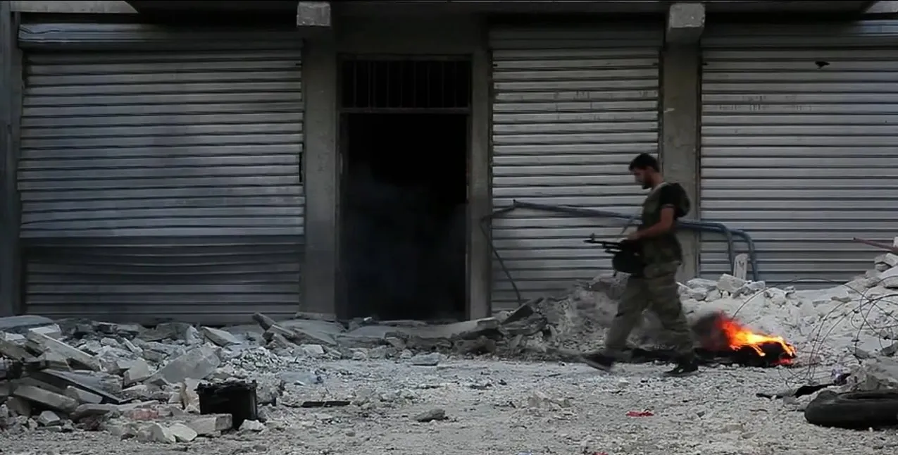 A fighter walking through rubble past shuttered storefronts in Aleppo, Syria, 2012.
